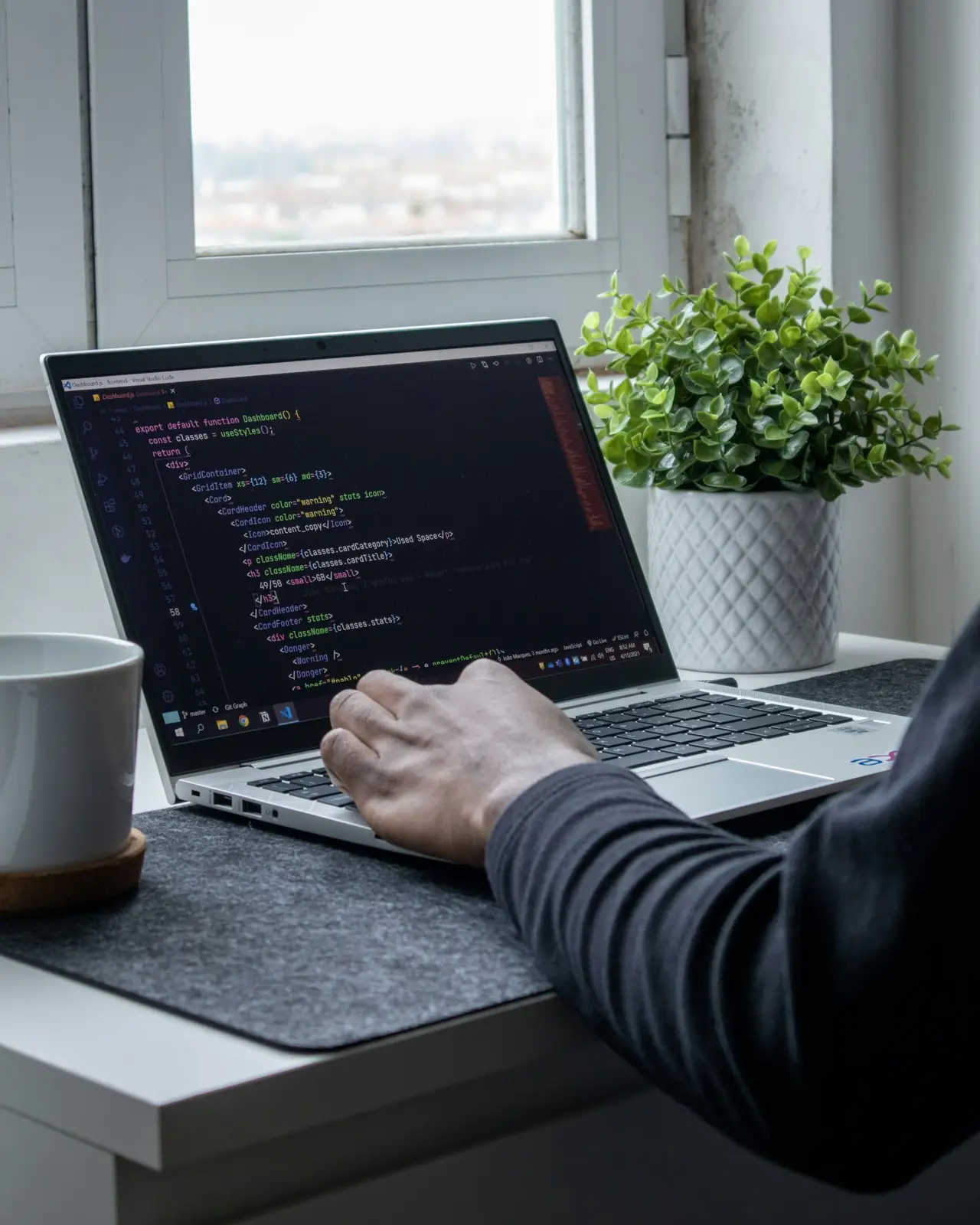 Developer writing code on a laptop at a desk with a plant